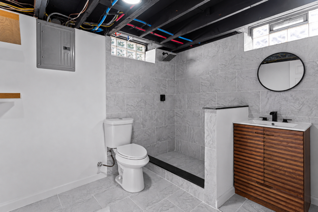 Finished basement bathroom with gray tile walk-in shower and wood vanity