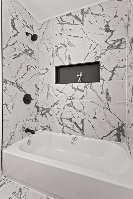 Finished bathroom tub and shower with black marble tile and matte black fixtures