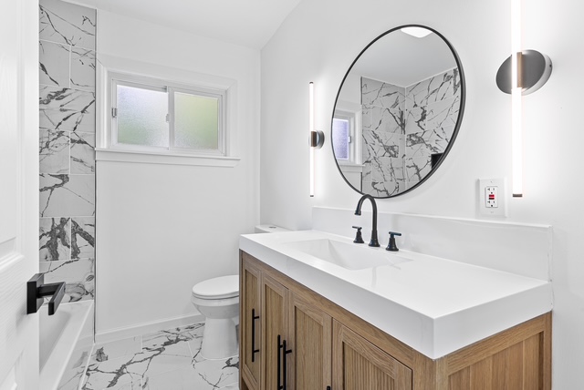 Finished bathroom with marble tile, wood vanity, and round mirror