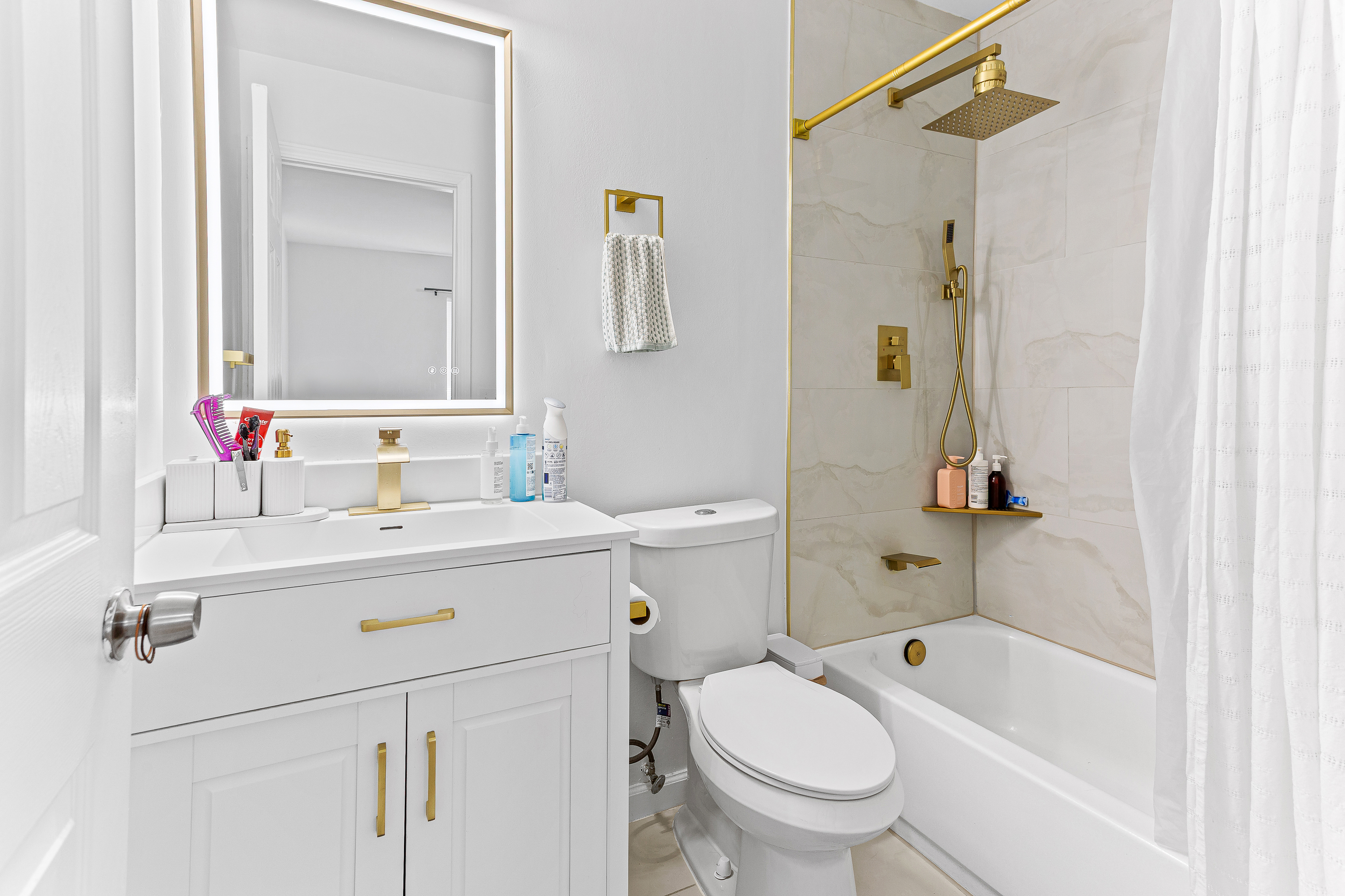 Finished bathroom with marble tile tub surround, gold fixtures, and backlit mirror