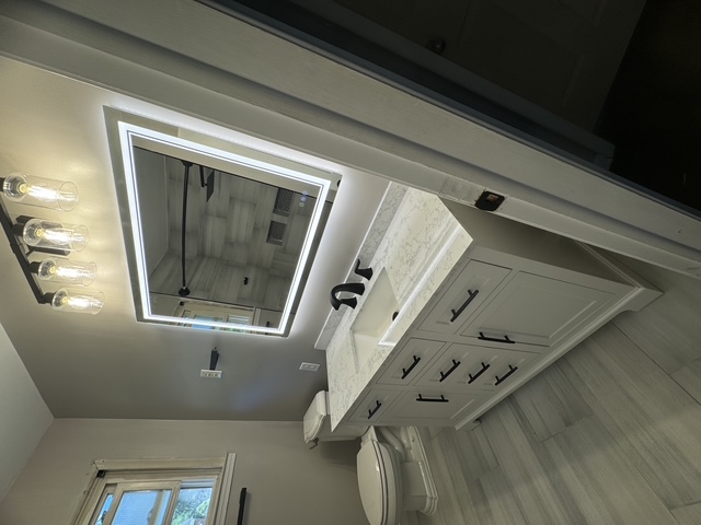 Finished bathroom with white shaker vanity, marble countertop, and backlit mirror