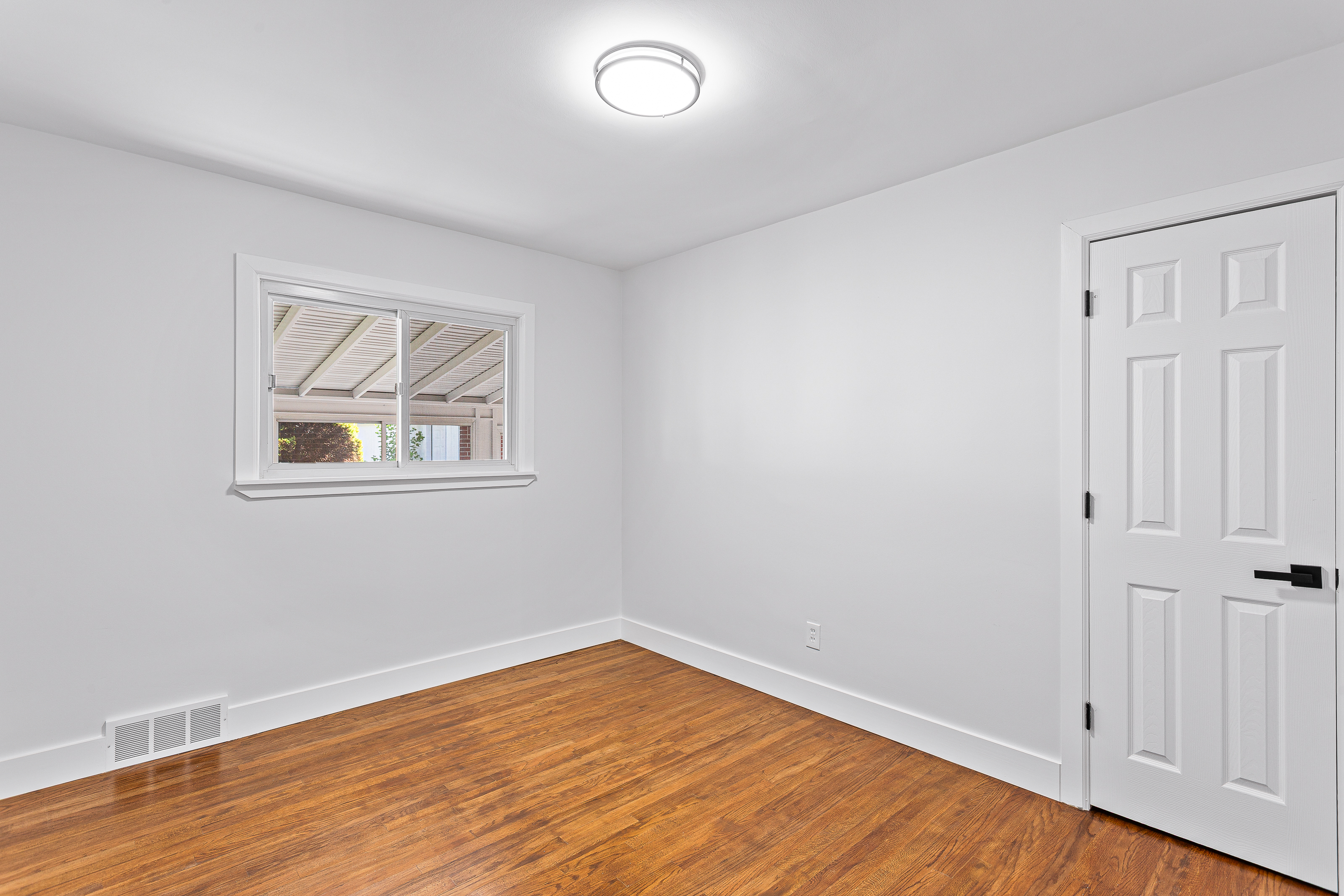 Finished bedroom with new hardwood flooring, white walls, and updated door and light fixture