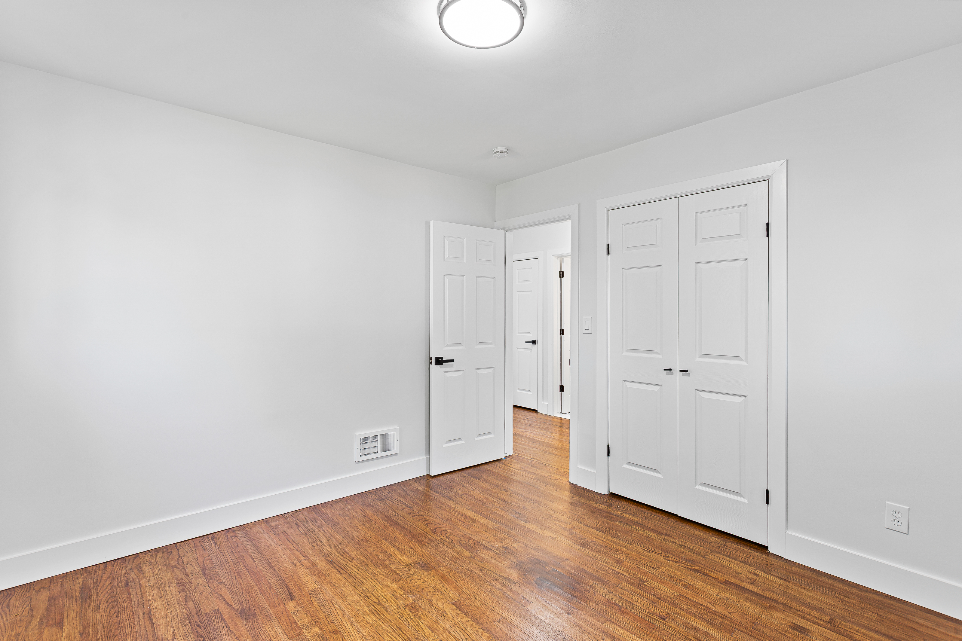 Finished bedroom hallway with closet doors and refinished hardwood flooring