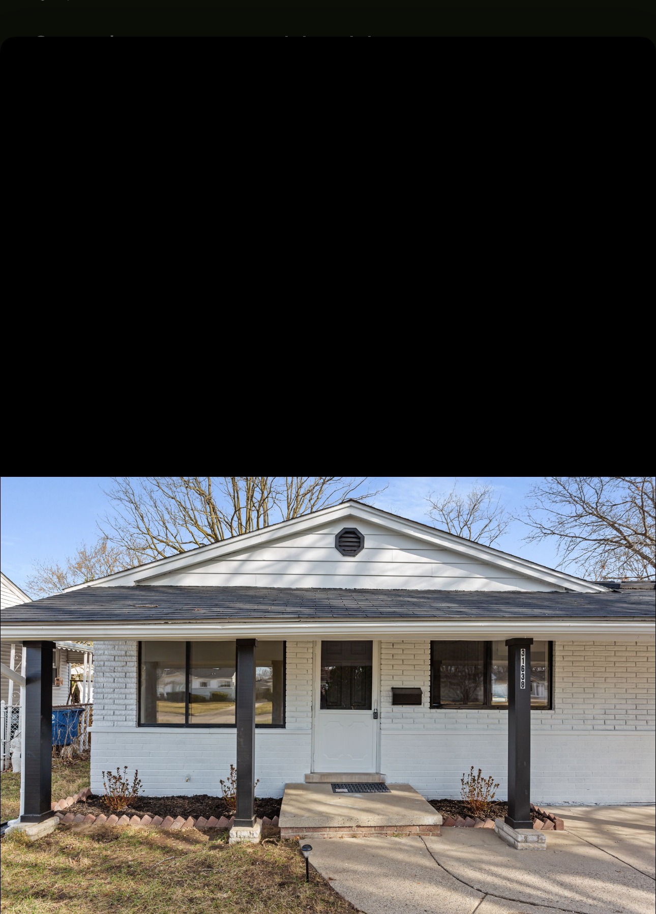 House exterior after renovation with white brick, black trim, and new porch posts