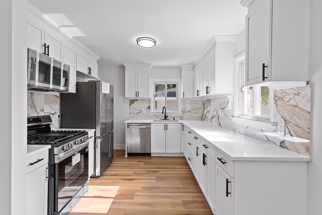 Finished kitchen with white shaker cabinets, marble backsplash, and stainless appliances