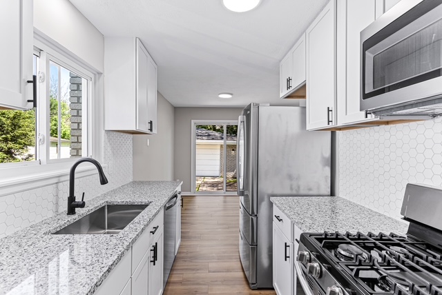 Finished galley kitchen with white cabinets, quartz counters, and stainless appliances
