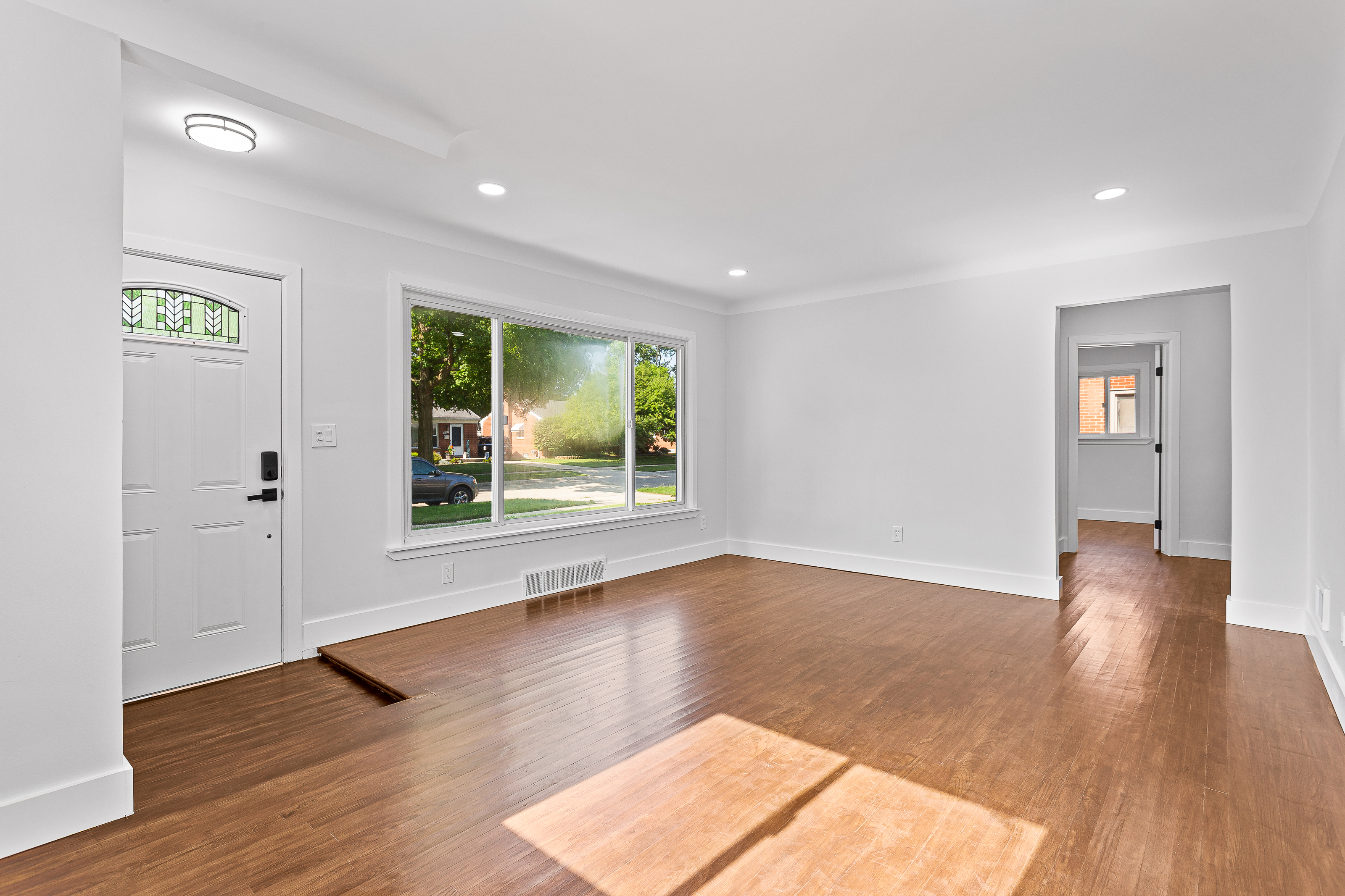 Finished living room with refinished hardwood flooring, fresh paint, and recessed lighting